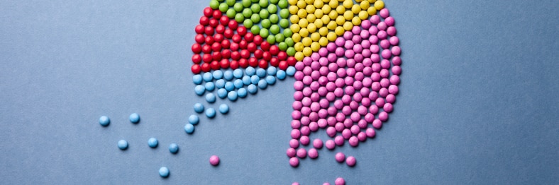 A pie chart made of colorful small round candies on a gray surface.
