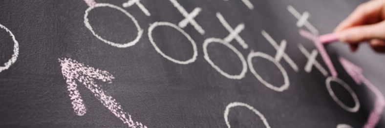 A chalkboard with circles and crosses drawn, while a hand uses pink chalk.